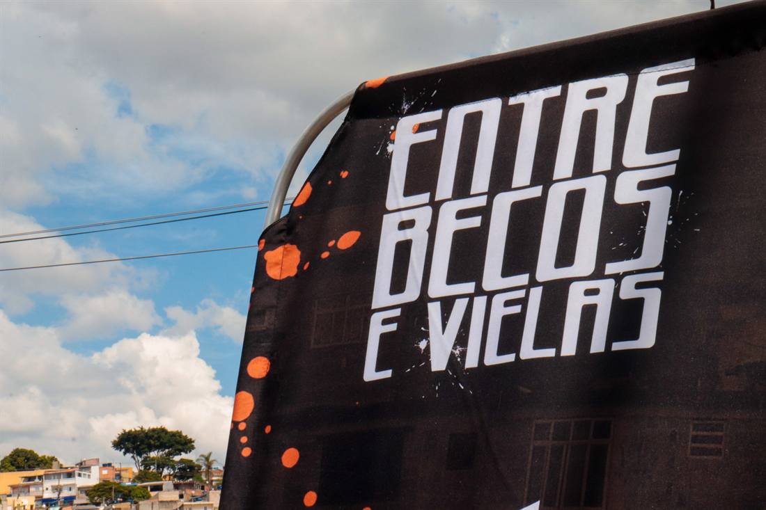 Bandeira do Entre Becos e Vielas, com respingos de tinta laranja, contra o céu da quebrada.