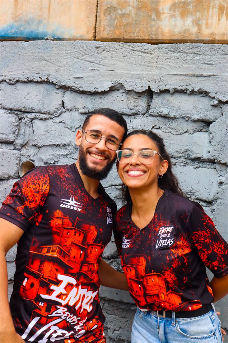 Casal sorrindo com as camisetas do projeto diante de um muro grafitado.